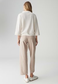 Roomwit geribd trui met lange mouwen, gecombineerd met losse, lichtbeige broek en witte sneakers. Geen patronen of opvallende hardware zichtbaar.