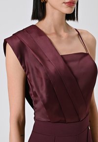 Robe en satin bordeaux avec un design à une épaule, des détails plissés et un corsage ajusté avec une texture lisse.