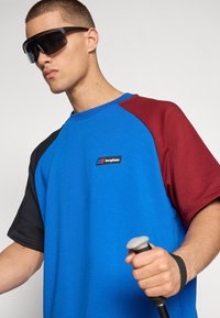 Blue, black, and burgundy color-blocked short-sleeve t-shirt with round neckline, featuring a small logo on the chest. Smooth fabric texture.
