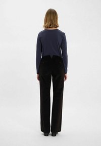 Haut à manches longues bleu marine associé à un pantalon à corduroy noir taille haute. Le haut a un col rond ; le pantalon possède deux poches à l'arrière.