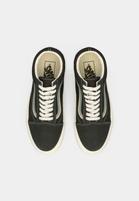 Pair of black Vans sneakers with white laces and soles, featuring green and beige side stripes, viewed from above on white background.