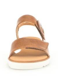 Brown leather sandal with two wide straps, a white sole, and a circular silver accent on the side. Smooth texture with a flat design.