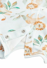 Combinaison bébé avec imprimé lion orange et feuille verte, dotée de boutons-pression argentés partiellement ouverts sur tissu blanc.