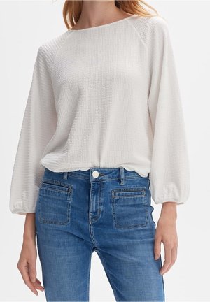 Witte textuur blouse met lange puffmouwen, gecombineerd met lichtblauwe hoge taille jeans met voor- en achterzakken.