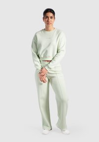 Vihreä vaaleanvihreä lyhyt huppari ja vastaavat leveät housut pehmeästä kankaasta, joissa on hienovaraisia ompelutietoja ja brodeerattu logo yläosassa.