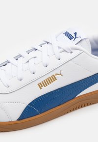 Puma sportcipő, fehér bőr felsőrésszel, kék részletekkel, arany logóval és barázdált gumitalppal, klasszikus fűzős kialakítással.