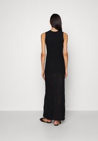 Robe maxi noire sans manches avec un motif en maille texturée, présentant un corsage ajusté et une jupe transparente et ample avec une silhouette longue.