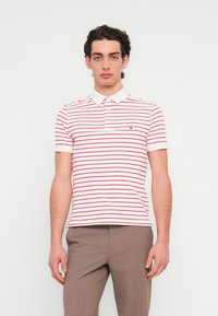 Πολο πουκάμισο με κόκκινες και λευκές ρίγες, με γιακά και κοντά μανίκια, στο στήθος διακοσμημένο με μικρό κεντημένο λογότυπο.