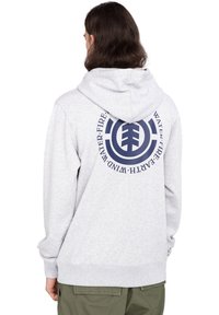Sudadera gris con capucha y un gran gráfico en azul marino en la parte posterior, con las palabras "AGUA, FUEGO, TIERRA, VIENTO" en un diseño circular.