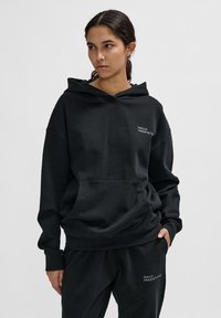 Czarna bluza z kapturem z miękkiego materiału, z przednią kieszenią i kapturem ze sznurkiem. Zawiera haft "HALO 19681972" w kolorze białym.