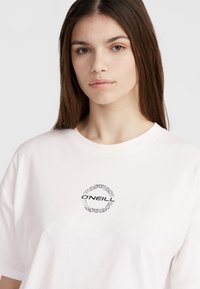 Hvid bomulds t-shirt med et cirkulært sort grafisk logo med indviklede mønsterdetaljer ved brystet. Rund halsudskæring og korte ærmer.