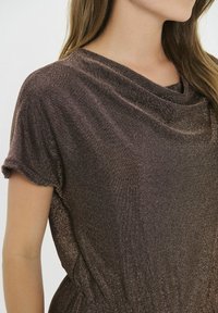 Bronzern színű ruha redőzött dekoltázzsal, rövid ujjal és puha, csillogó textúrával. Az övnél gyűrődött részletekkel rendelkezik.