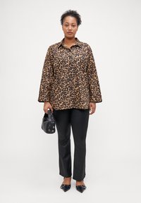 Chemise oversized en imprimé léopard marron et noir, associée à un pantalon noir ajusté et un sac à main noir. Talons aiguilles noirs avec clous.