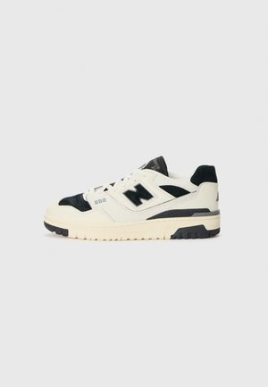 Baskets New Balance 550 blanches et noires vues de côté avec semelle crème et logo "N" noir sur un fond clair uni.
