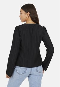 Top nero a maniche lunghe con righe verticali, scollatura rotonda e dettagli con spalle a sbuffo, abbinato a jeans a vita alta blu chiaro.