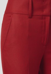 Czerwone spodnie z teksturowanej tkaniny z eleganckim pasem, bocznymi kieszeniami i subtelnymi detalami haftu, podkreślającymi dopasowany krój.
