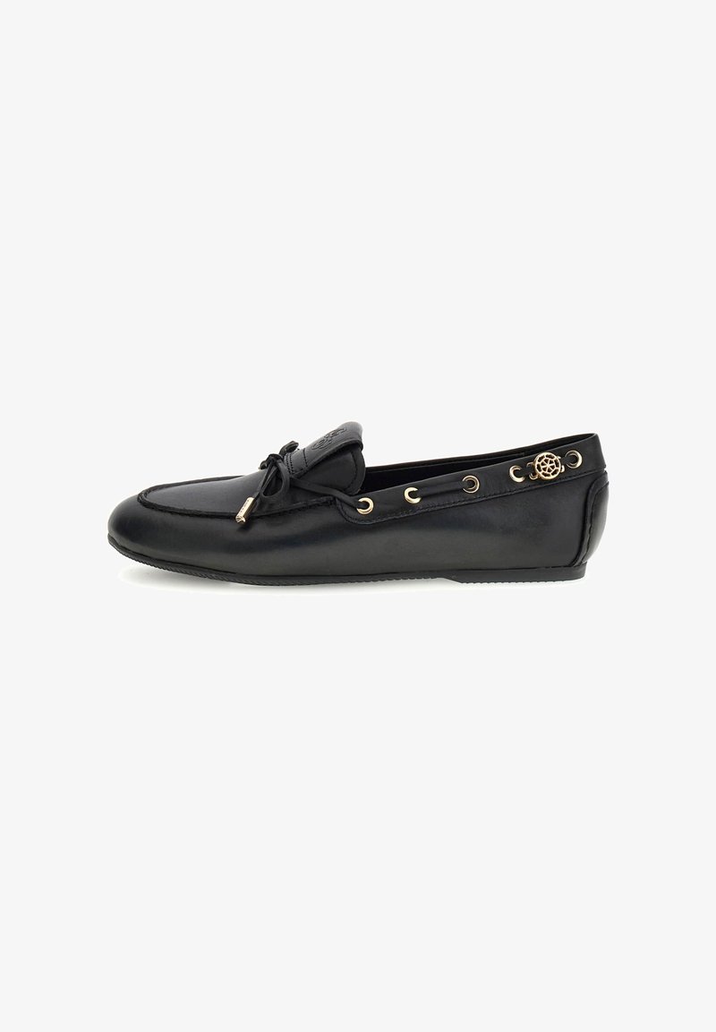 Mocassin en cuir noir avec lacets en forme de nœud papillon, œillets dorés et un emblème doré décoratif sur le côté, présenté en profil latéral.