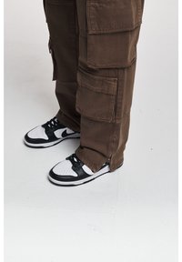 Bruna cargobyxor med flera fickor och en avsmalnande passform, tillsammans med svarta och vita Nike-sneakers med en låg profil.