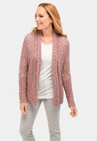 Lace-Cardigan in zartem Pink mit offenem Vorderteil, langen Ärmeln und strukturiertem Strickmuster. Kombiniert mit einem leichten Oberteil und grauen Hose.