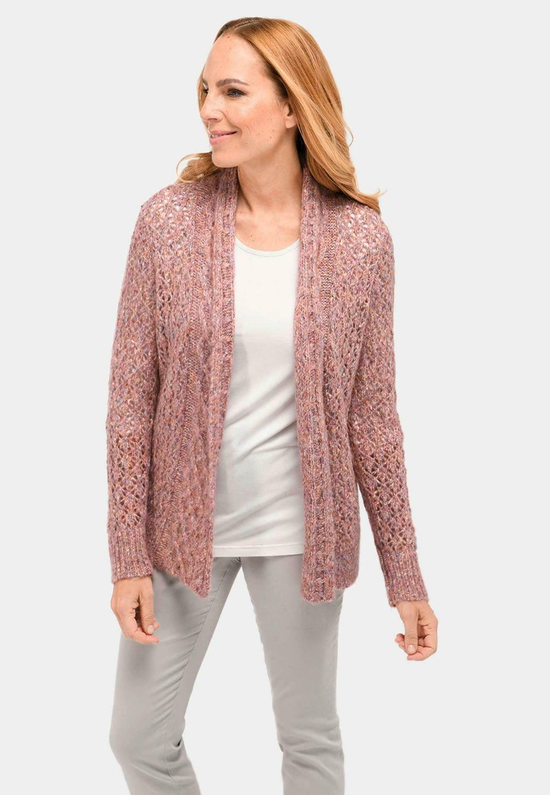 Lace-Cardigan in zartem Pink mit offenem Vorderteil, langen Ärmeln und strukturiertem Strickmuster. Kombiniert mit einem leichten Oberteil und grauen Hose.