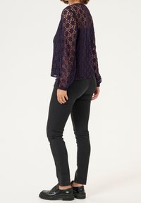 Haut en dentelle bleu marine à manches longues, motif floral et coupe ample, assorti à un jean skinny noir et des mocassins noirs.