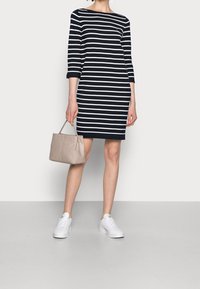 Robe rayée marine et blanche à manches trois-quarts, coupe ajustée. Associée à un sac à main beige et des baskets blanches.