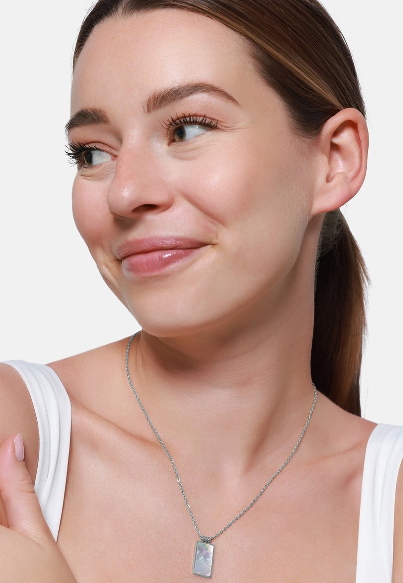 Collana d'argento con pendente rettangolare dalla superficie texturizzata, indossata su una spalla nuda, su uno sfondo bianco.