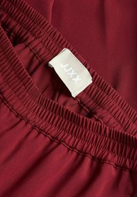 Bordo tkanina z mehko teksturo, z elastičnim pasom in oznako "JUXX", prišito v beli barvi.