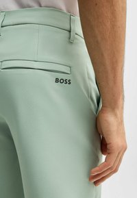 Light green trousers featuring a smooth texture, back pocket, and a visible black "BOSS" logo on the right side.