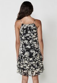 Schwarz-creamfarbenes gemustertes Kleid mit gerafftem Saum, dünnen verstellbaren Trägern und einem leichten, strukturierten Stoff.