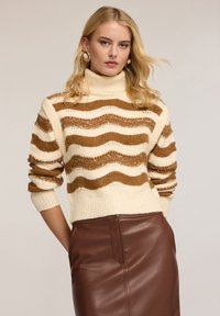 Sweter w paski w odcieniach kremu i brązu z teksturowym wykończeniem; połączony z brązową skórzaną spódnicą z boczną kieszenią.