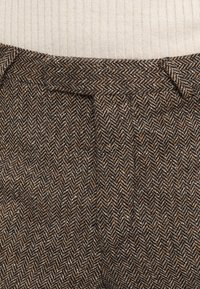Herringbone-patterned trousers in brown and beige tones, featuring a textured fabric, pleats at the waist, and a fitted design.
