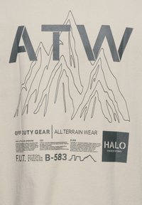 Hvid bomulds t-shirt med sorte grafik: stort "ATW," bjergdesigns og tekst om fritidstøj og fysisk træning nedenunder.