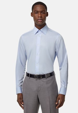 Camisa de vestir de manga larga azul claro con cuello botón, textura suave y botones a juego, combinada con pantalones gris con rayas y un cinturón negro.
