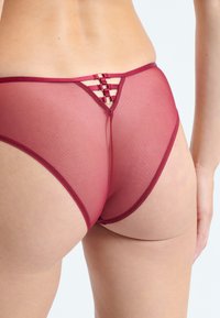 Lingerie trasparente borgogna con un unico design incrociato sul retro, caratterizzata da dettagli in satin e tessuto morbido e traslucido.