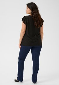 Top negro con mangas cortas con volantes y detalle de ojales, combinado con jeans acampanados azul oscuro y tacones negros de punta.