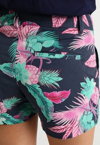 Shorts à imprimé floral avec une base bleu marine foncé ornée de motifs tropicaux roses et verts, tissu texturé et détail de poche arrière.