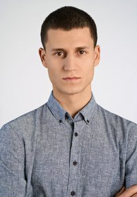 Jasnoniebieska, krótko rękawowa koszula z guzikami o teksturowanej tkaninie, z kołnierzykiem i ciemnymi guzikami, noszona przez osobę z krótkimi włosami.