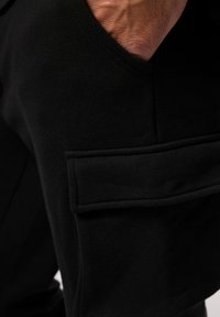 Schwarze Cargo-Hosen mit einer seitlichen Tasche und Klappe. Hergestellt aus weichem Stoff mit glatter Textur. Taillierte Passform um die Hüfte.