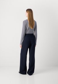 Haut à manches longues rayé en bleu marine et blanc, assorti à un pantalon large bleu marine. Tissu lisse, ajusté à la taille et coupe décontractée dans l'ensemble.