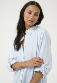 Ljusblå button-up skjorta med strukturerad tyg, uppvikta ärmar och krage. Har knappar framtill och en avslappnad passform.