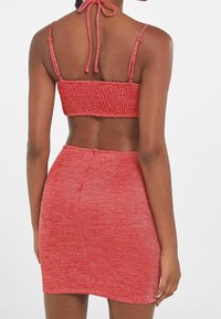 Punainen ribattu crop-top, jossa on ohuet hihnat ja solmu takana, yhdistetty kireästi istuvaan punaiseen hameeseen. Materiaalissa on hieman hohdetta.