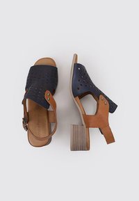 Sandales à talons avec une tige perforée bleu marine et des accents en cuir beige. Talon bloc avec un design texturé. Bride de cheville ajustable.