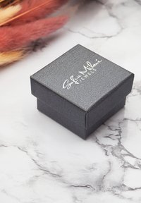 Svart, texturerad smyckesbox med lock, prydd med präglad silvertext för "Sofia Milani Jewels." placerad på en marmorlika yta.