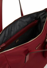 Sac à main synthétique rouge avec fermeture éclair dorée, doublure intérieure noire présentant un motif de logo répété, et deux poches intérieures, dont une zippée.