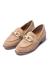 Beige suède loafers met een ronde neus, voorzien van een gouden hardware detail aan de voorkant en een lage, platte bruine hak.