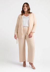 Completo a due pezzi composto da un giubbotto beige chiaro, leggermente texturizzato, con maniche lunghe e pantaloni palazzo abbinati, tutti con una finitura scintillante.