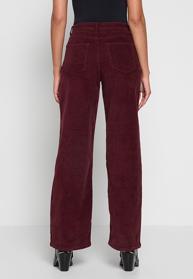 Burgundy wijde corduroy broek met verticale ribbels, twee achterzakken en een hoge taille, gecombineerd met zwarte enkellaarsjes.