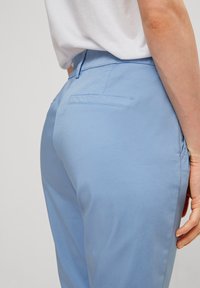 Ljust blå byxor med en slät yta, med en bakficka och en figurnära midja. Designen betonar en skräddarsydd silhuett.