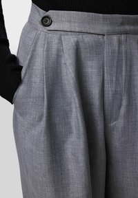 Szare spodnie z mieszanki lnu o luźnym kroju, z przodu z zakładkami i czarnym guzikiem w talii. Posiadają boczne kieszenie.